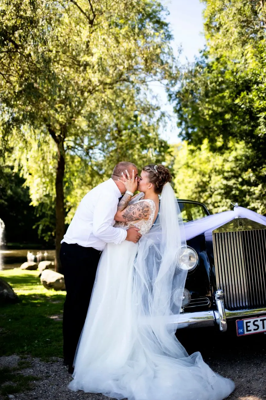 A bride and groom kiss beside a vintage Rolls-Royce
